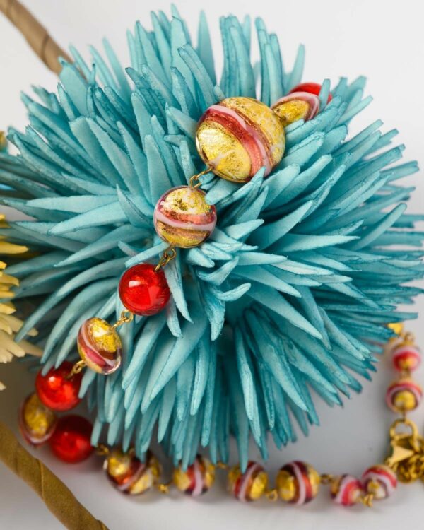 Close-up of a Murano necklace with red and gold beads displayed on a blue decorative piece